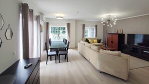 A modern living room with a dining area, a sofa, a TV, and a large window with curtains.