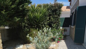A paved courtyard with a mix of gravel and cobblestone flooring, surrounded by various plants and shrubs.