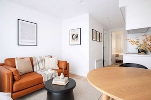 A modern living room with a brown leather sofa, a round wooden dining table, and framed artwork on the walls.