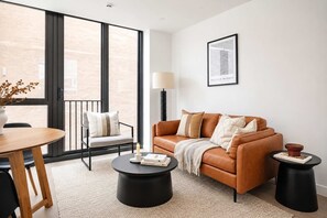 A modern living room with a leather sofa, a round coffee table, a dining table, and a chair. There is a framed picture on the wall and a vase with dried flowers on the table. - Stylish 1BR | Pool + Gym | Courtenay (Wellington)