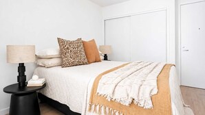 Ein Schlafzimmer mit einem Bett, zwei Nachttischen, einer Lampe, einer Tür und einer Wand.
