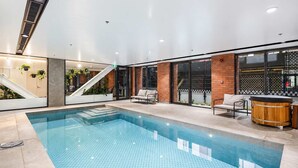 Ein Hallenbad mit Fliesenboden, einer Holz-Whirlpool und einer Sitzecke mit einer Couch und Sesseln.