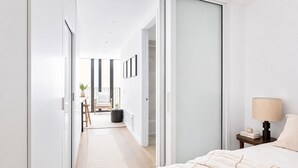 Ein modernes Schlafzimmer mit Bett, Nachttisch, Lampe und Blick in einen Essbereich mit Stuhl und Tisch.