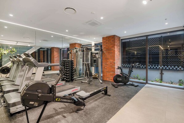 Un gimnasio moderno con máquinas de cardio, equipo de levantamiento de pesas y un amplio ventanal que proporciona luz natural.