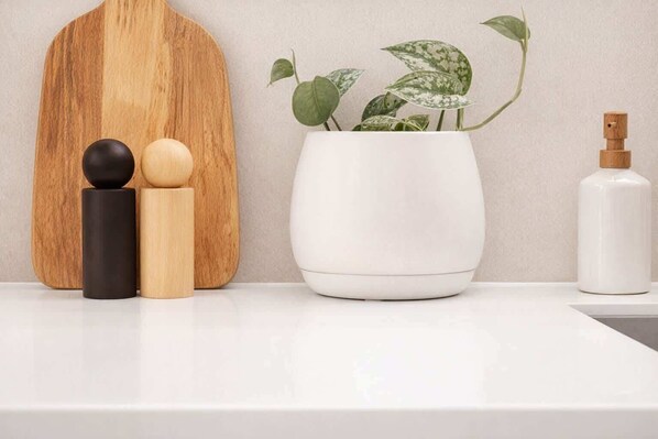 Una encimera blanca con una tabla de madera, una planta en maceta y una botella blanca.