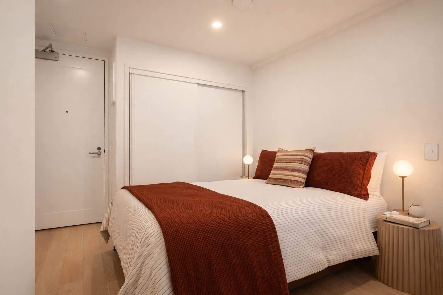 A bedroom with a bed, bedside lamps, and a door.