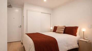 A bedroom with a bed, bedside lamps, and a door.