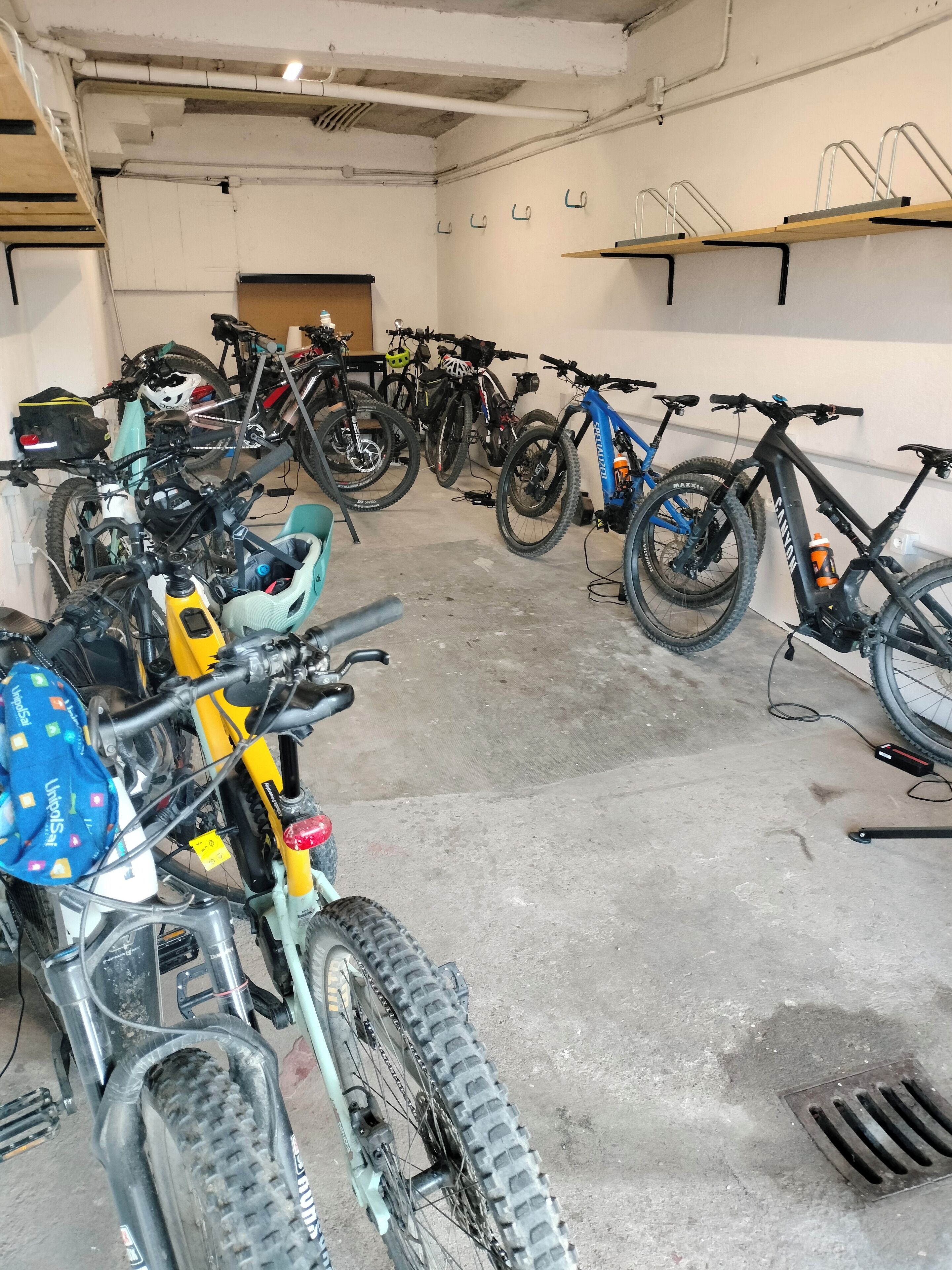 Zona de guardado para bicicletas con varias bicicletas, suelo de hormigón y tuberías aéreas.