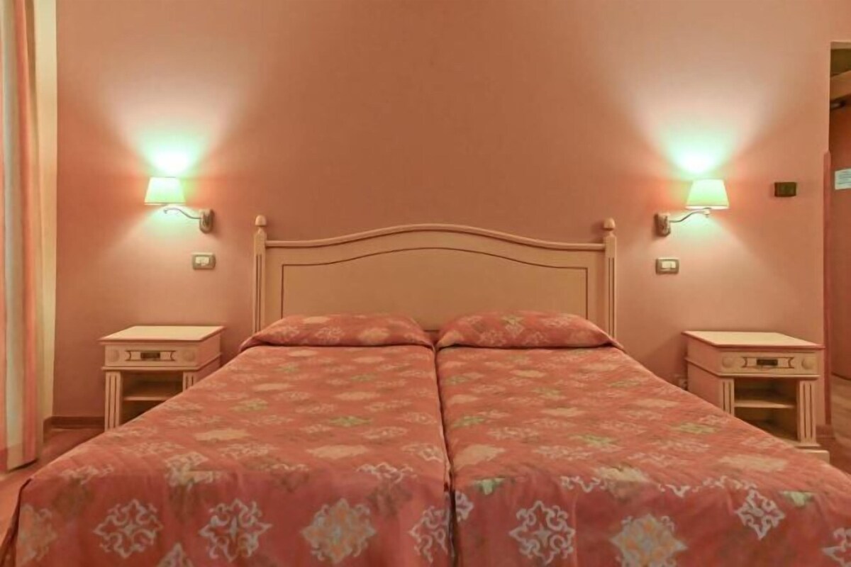 Een tweepersoonsbed met hoofdeinde, twee nachtkastjes en wandlampen.