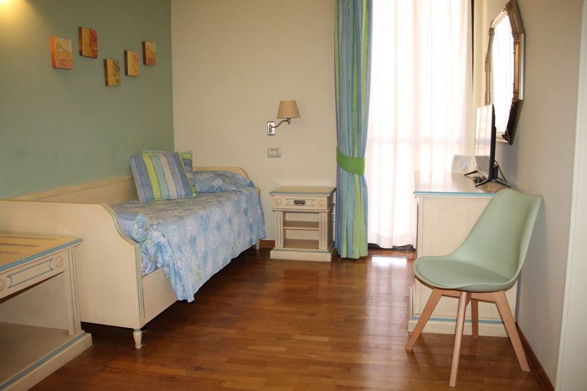 A bedroom with a bed, bedside table, chair, and a wall-mounted lamp.