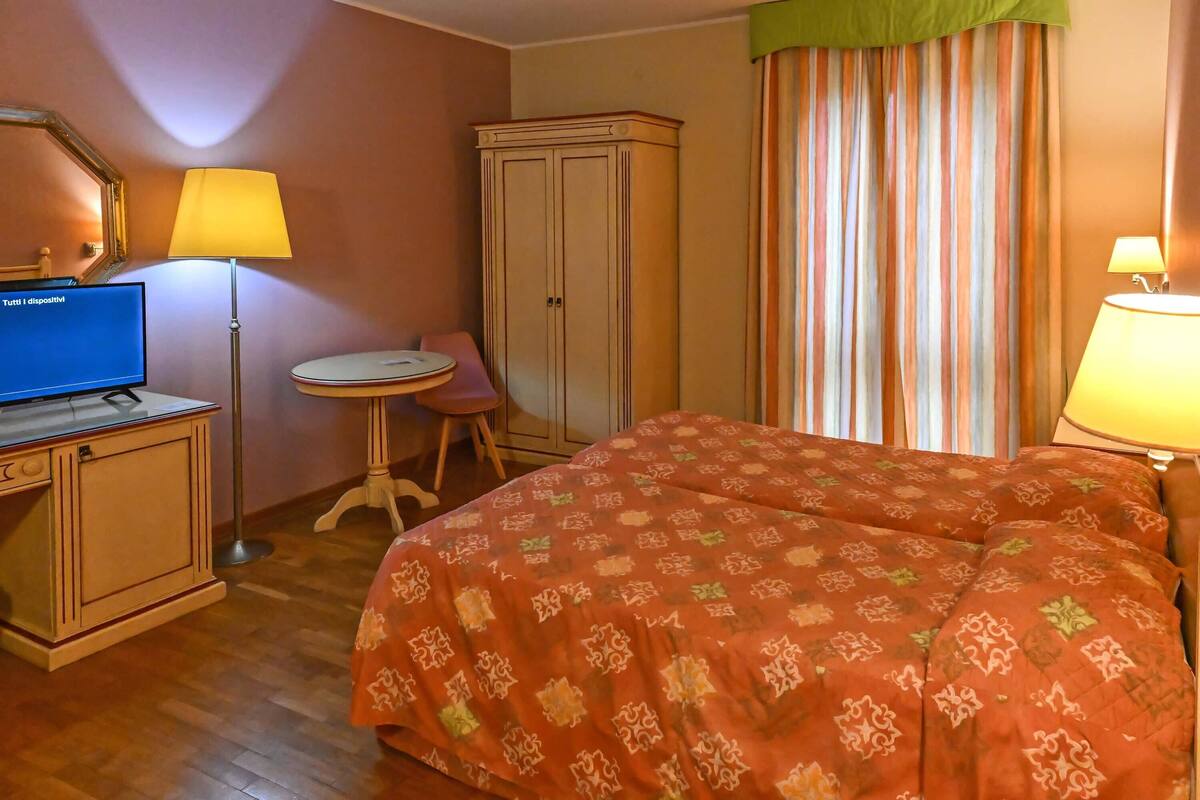 A hotel room with a bed, a desk with a computer, a chair, a wardrobe, and a window with curtains.