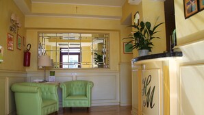 Une pièce avec deux fauteuils verts, un miroir, une plante en pot et un buffet de couleur crème orné d’un monogramme.