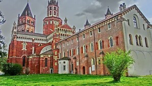 Un bâtiment historique doté d’une tour imposante et de fenêtres en arc de cercle, entouré d’une pelouse bien entretenue.