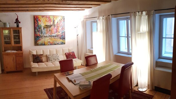Ett mysigt vardagsrum med ett träpanelat tak, en vit soffa, ett matbord med röda stolar och en färgstark, abstrakt målning på väggen.