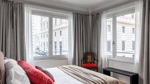 A hotel room with a large bed, a bench, and a chair by the window.