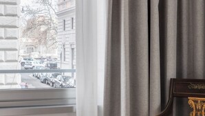 A hotel room with a bed, a chair, and a view of the street through a window with curtains.