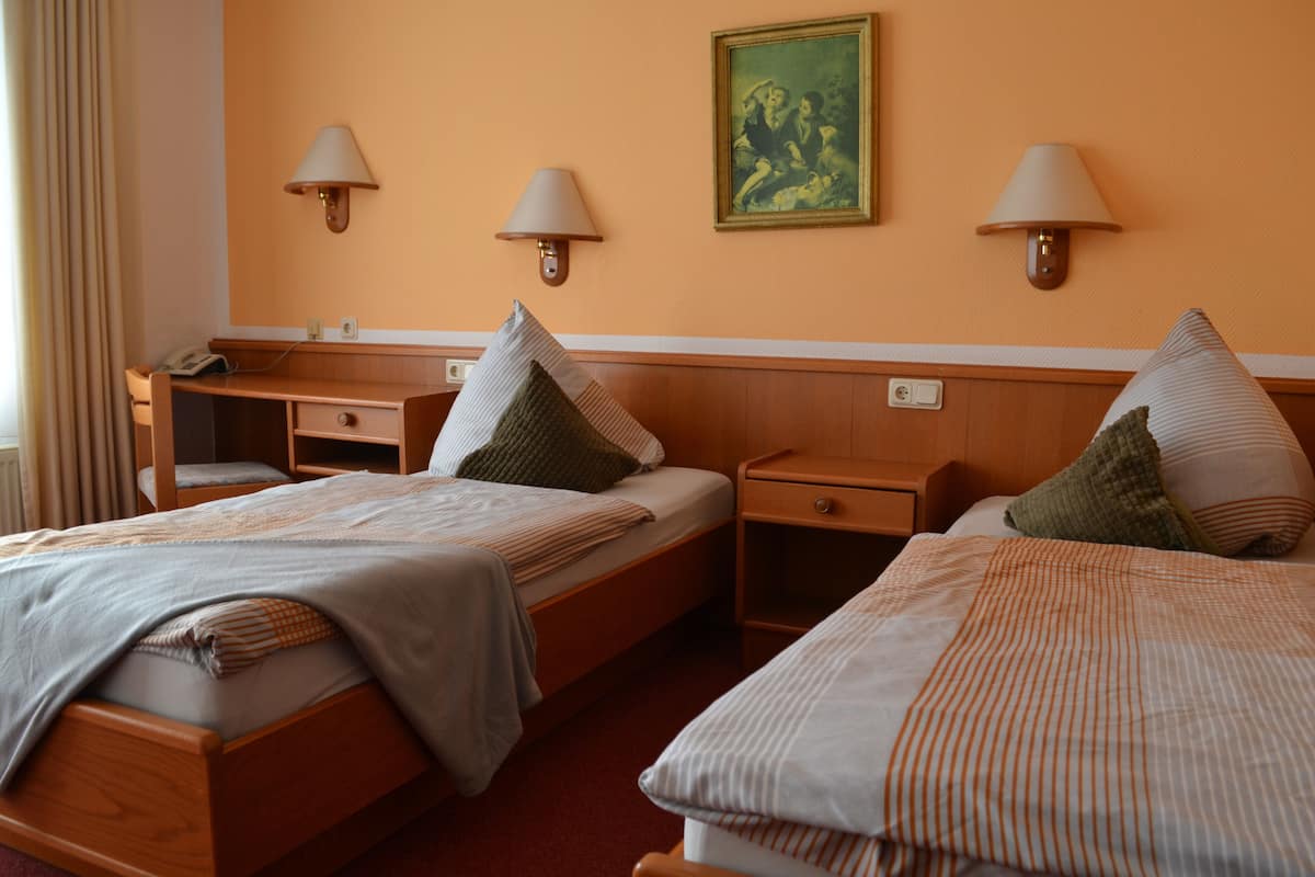A hotel room with two beds, a desk, and two wall-mounted lamps.