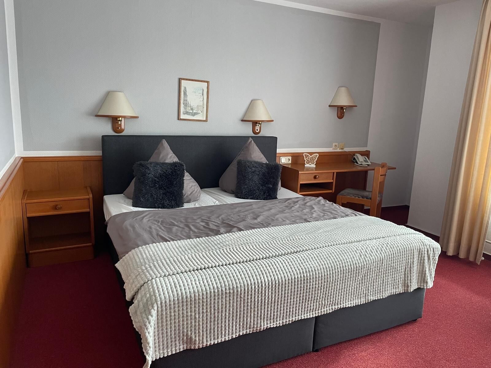 Habitación de hotel con una cama grande, dos mesitas de noche, un escritorio con una silla y dos lámparas de pared.