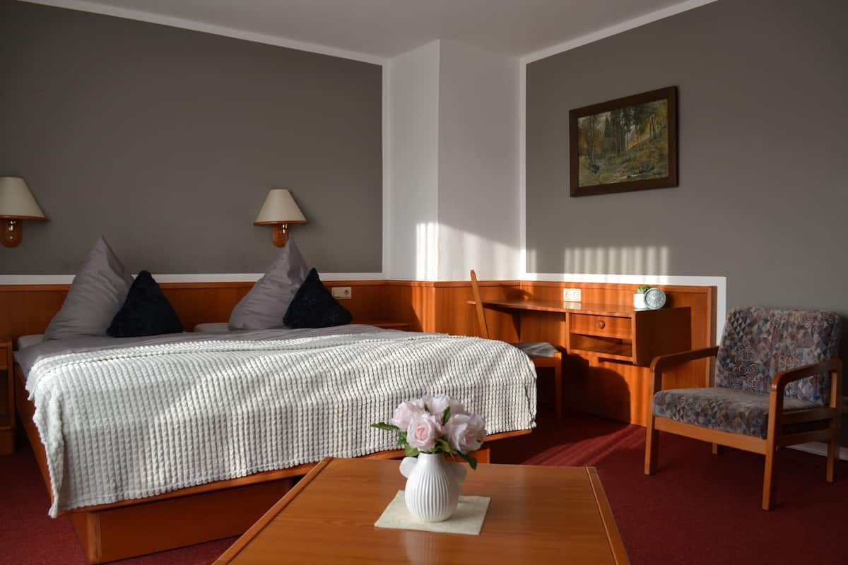 A hotel room with a bed, bedside lamps, a chair, a small table, and a painting on the wall.