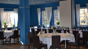 A dining area with tables set for service, blue walls, and large windows with white curtains. - Hotel Blocksberg (Wernigerode)