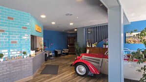 A reception area with a blue-tiled wall, a reception desk, a vintage car, and a wooden floor. - Hotel Blocksberg (Wernigerode)