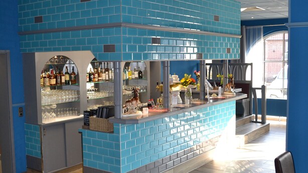 A bar area with blue tiled walls, wooden flooring, and a counter with various bottles and glasses. - Hotel Blocksberg (Wernigerode)