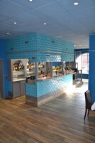 Uma área de bar com paredes azulejadas em azul, piso de madeira e um balcão com diversos copos e garrafas.