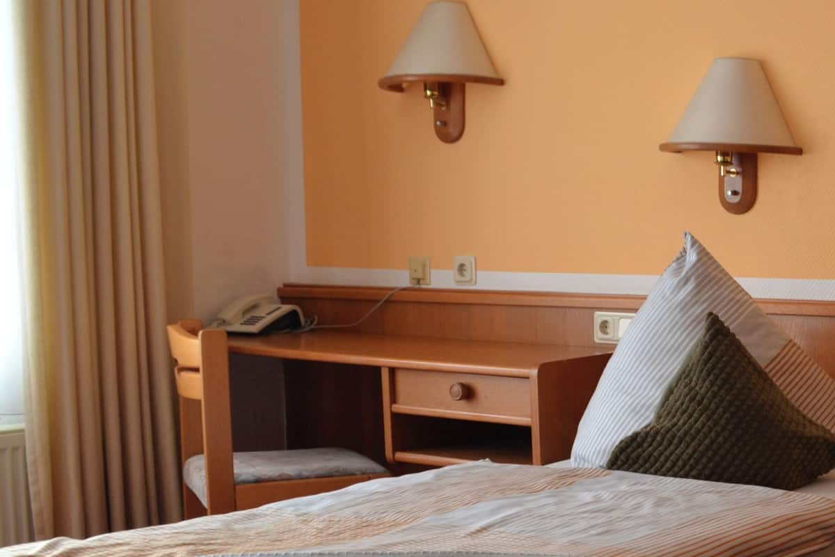 A hotel room with a bed, a desk, and two wall-mounted lamps.