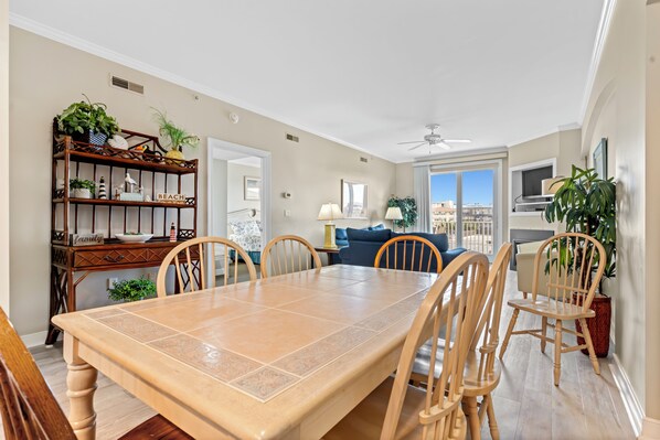 A dining area with a large table, chairs, a wooden sideboard with plants, and a view of the outdoors.