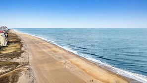 A coastal view with a sandy beach, ocean waves, and a building with a flag.
