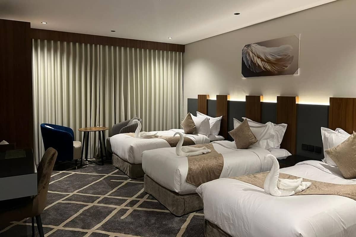 A hotel room with three beds, a desk, a chair, and a large window with curtains.