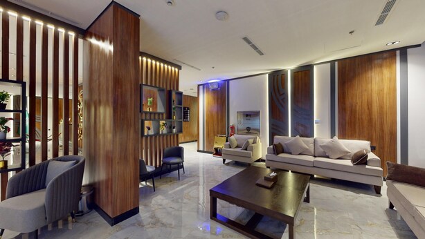 A modern living room with a sofa, armchairs, and a coffee table. There are wooden panels and a fire extinguisher visible. - How inn Hotel (Madinah)