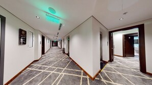 A hotel corridor with a patterned carpet, white walls, and doors leading to rooms. - How inn Hotel (Madinah)