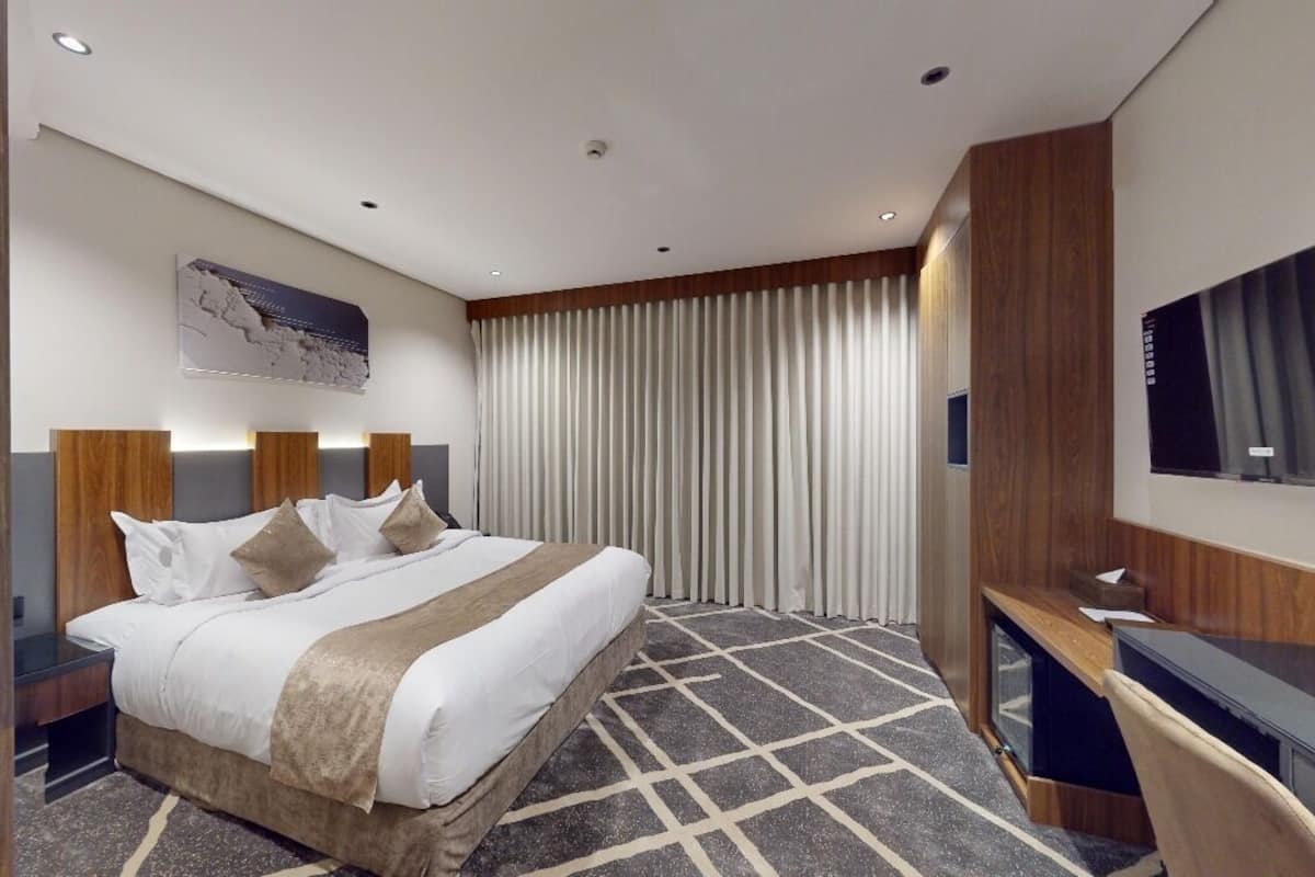A modern hotel room with a large bed, a desk, and a TV.