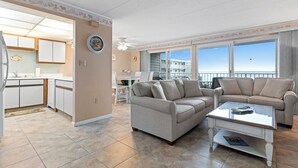 En rummelig stue med et beige sofasæt, et sofabord og havudsigt gennem store vinduer.
