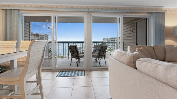 En balkon med spisebord og stole, en sofa og udsigt til havet og bygninger.