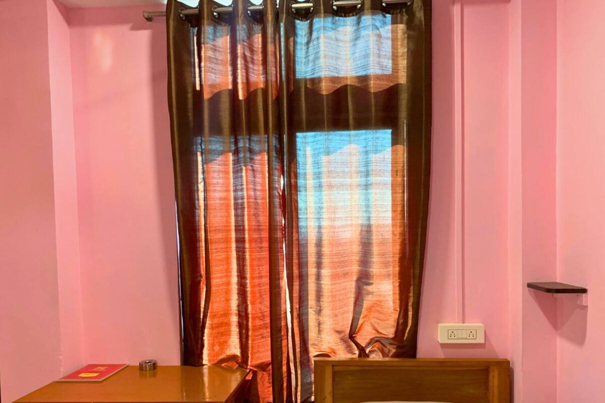 A room with a bed, a wooden desk, a green chair, and a window with orange curtains.