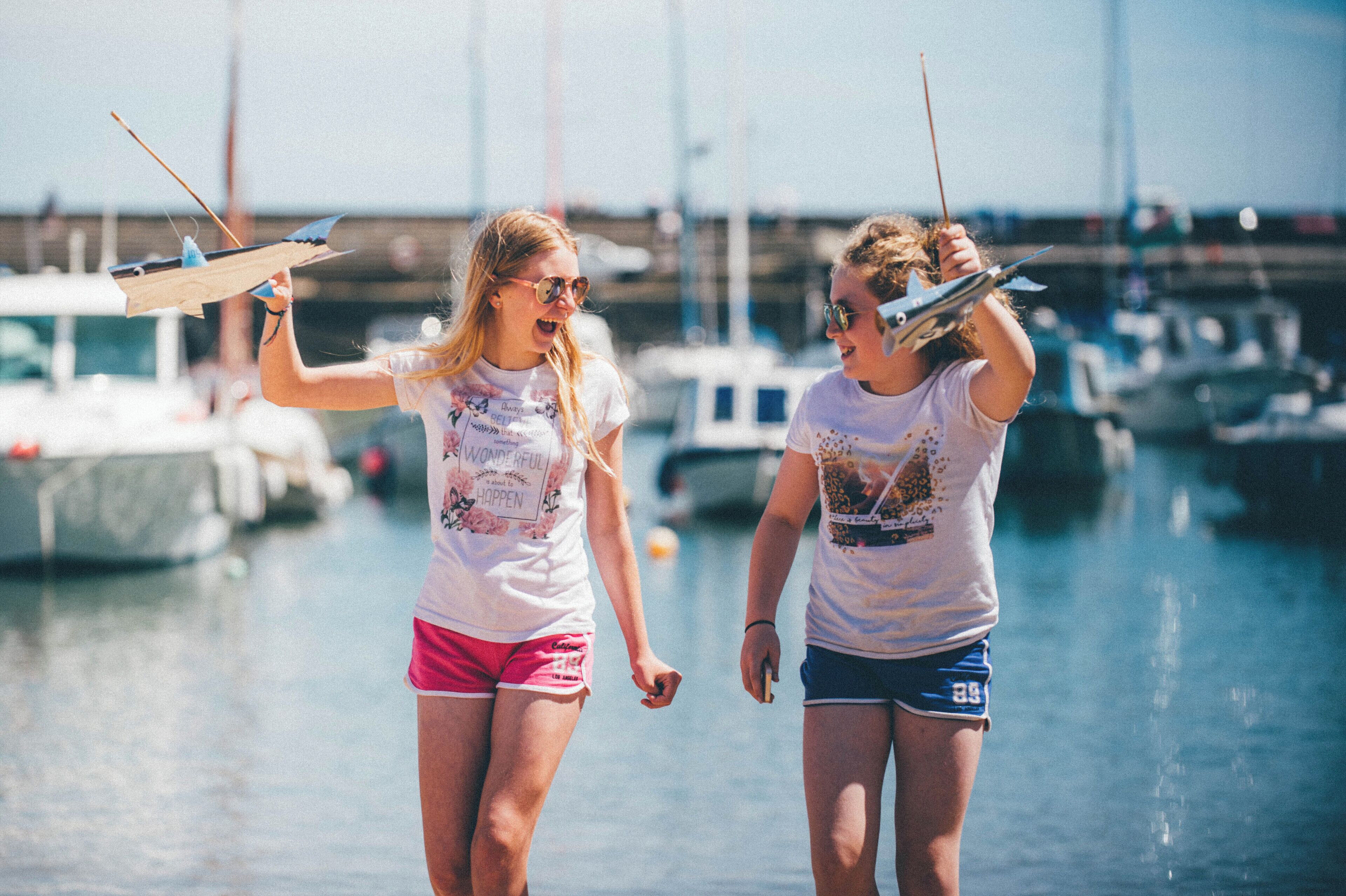 Two people holding kites at a marina with boats in the background.