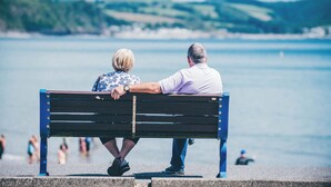 Un couple est assis sur un banc, face à une étendue d’eau, avec une côte lointaine à l’horizon.