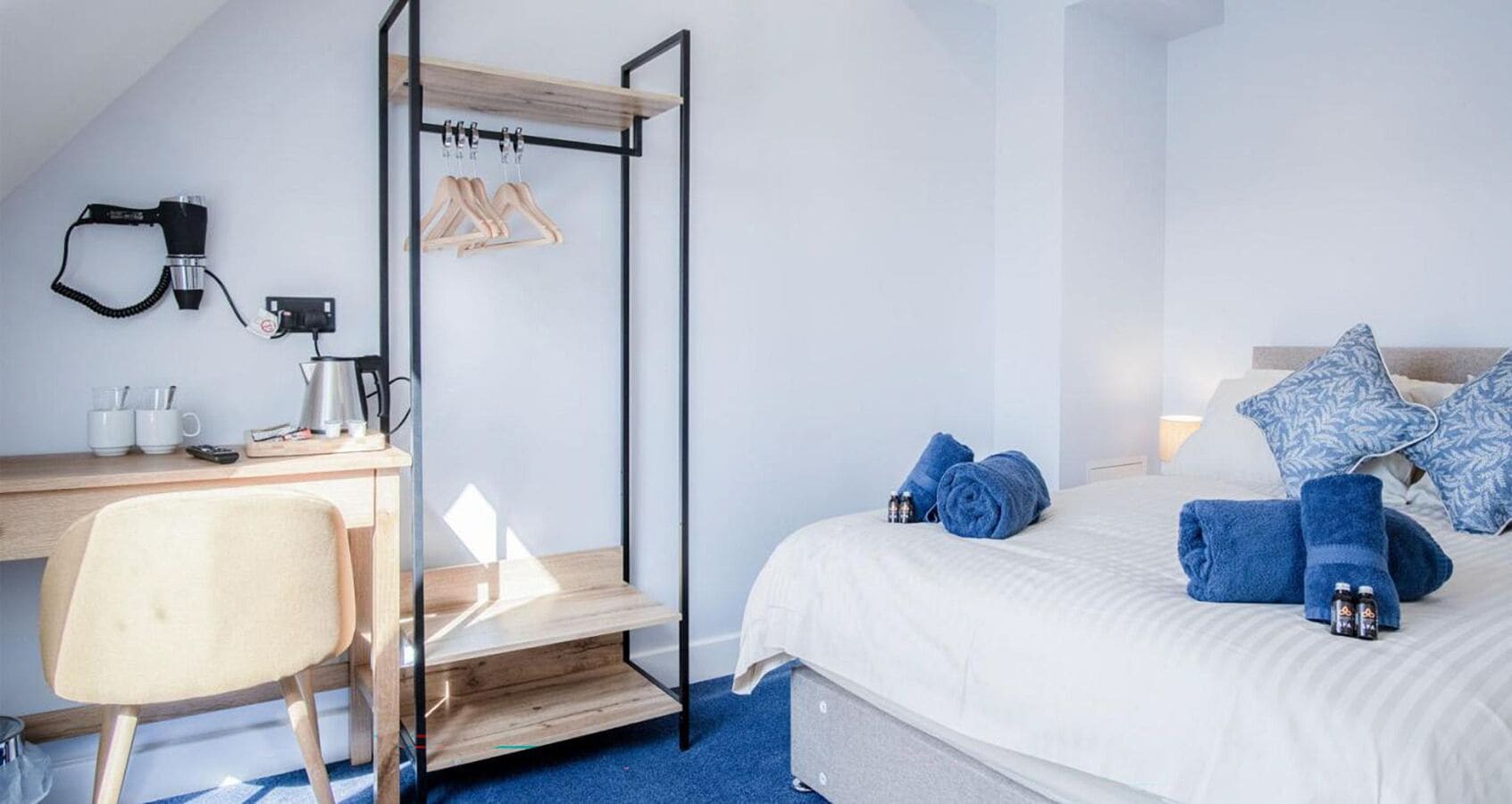 A bedroom with a bed, a desk, a chair, and a hanging clothes rack.