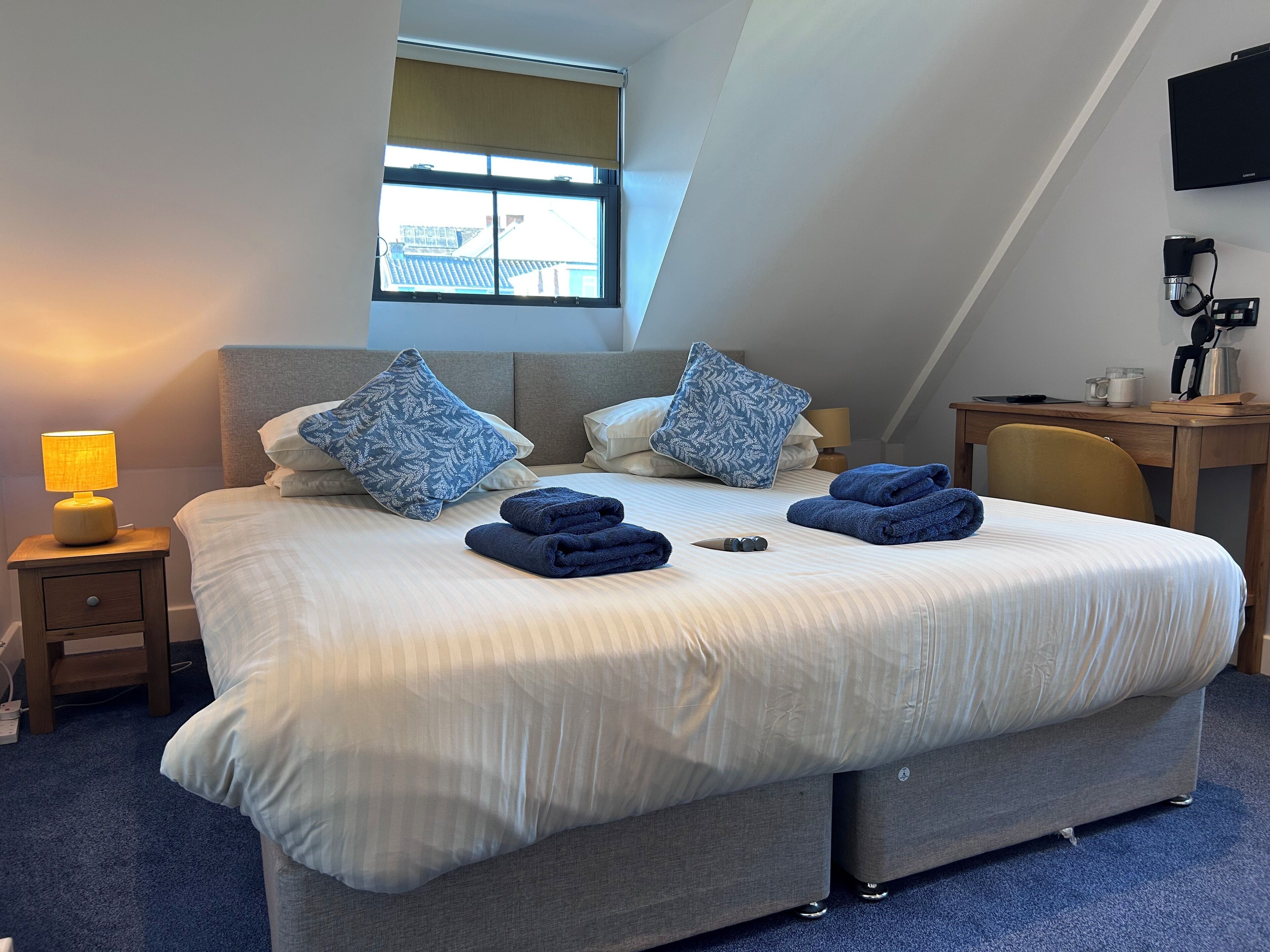 A neatly made bed with pillows, a lamp, and folded towels on a blue carpeted floor.