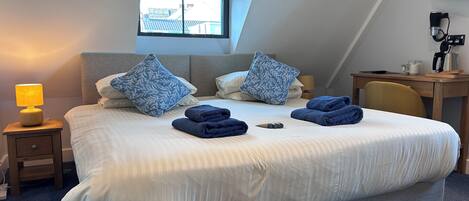 A neatly made bed with pillows, a lamp, and folded towels on a blue carpeted floor.