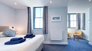 Ein Hotelzimmer mit einem Bett, zwei Fenstern mit Vorhängen, einem Heizkörper, einem kleinen Tisch und zwei Stühlen.