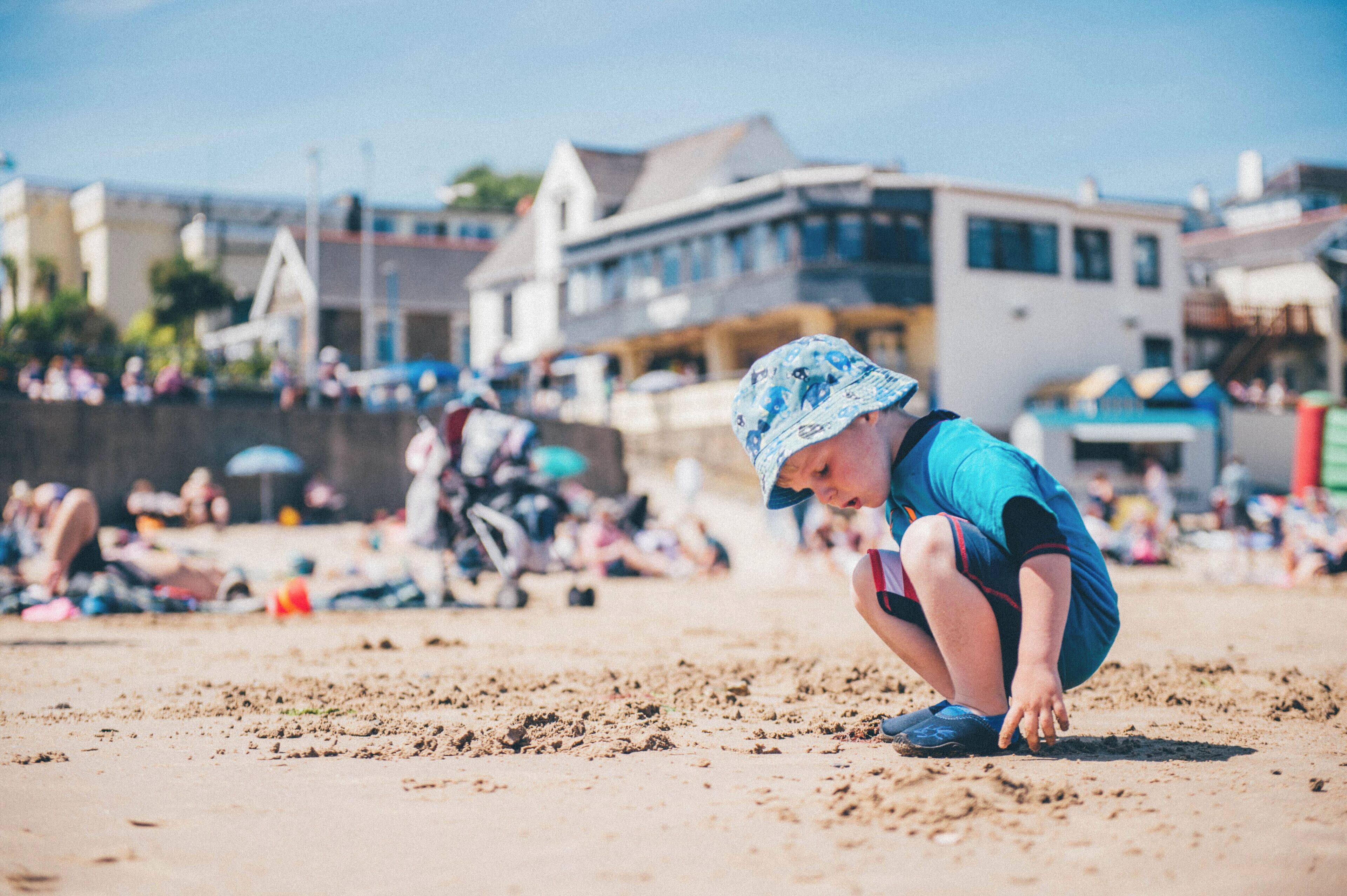 A child playing on a sandy beach with buildings in the background.