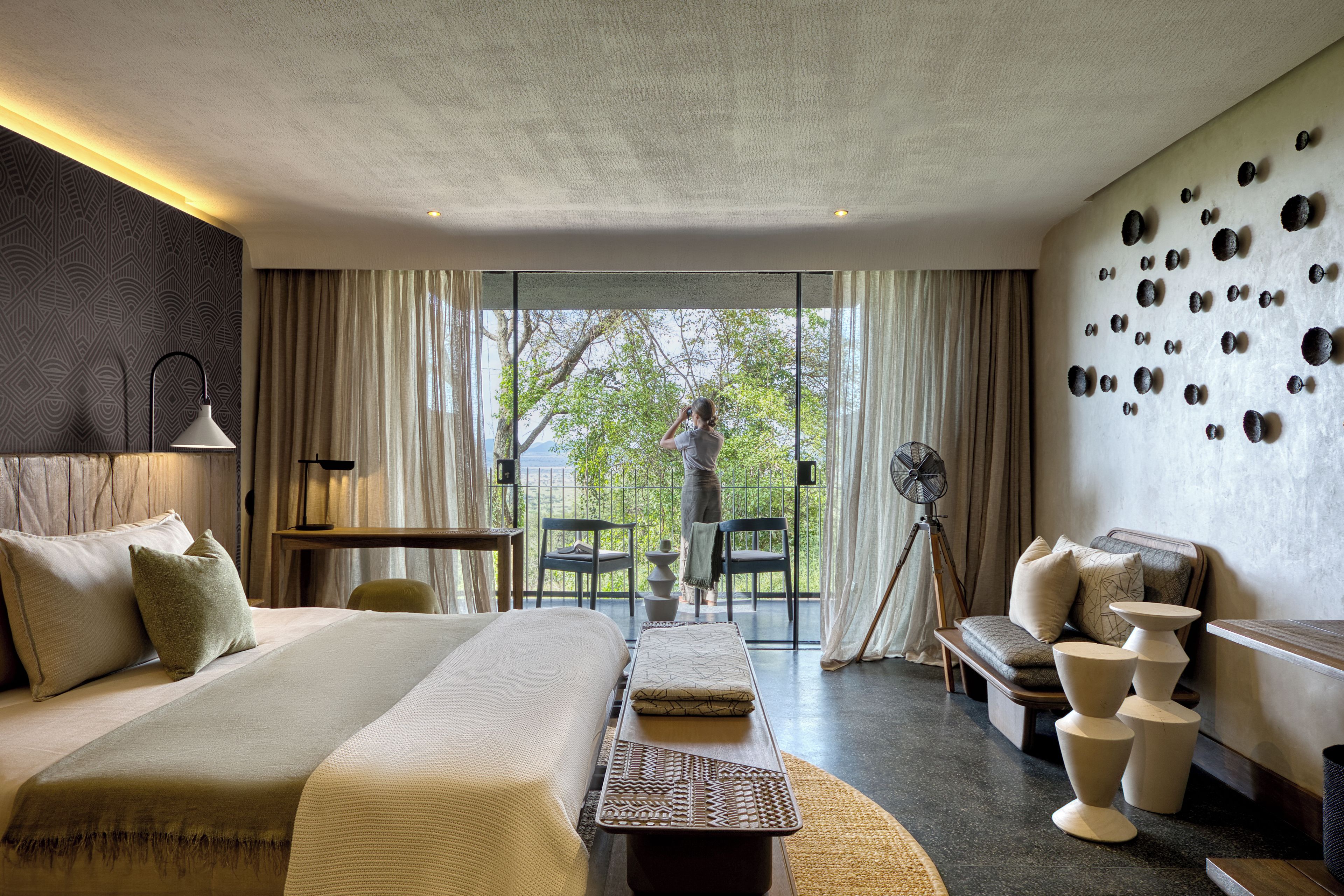 Une chambre d’hôtel avec un grand lit, un bureau, une chaise, un ventilateur et une vue sur l’extérieur.