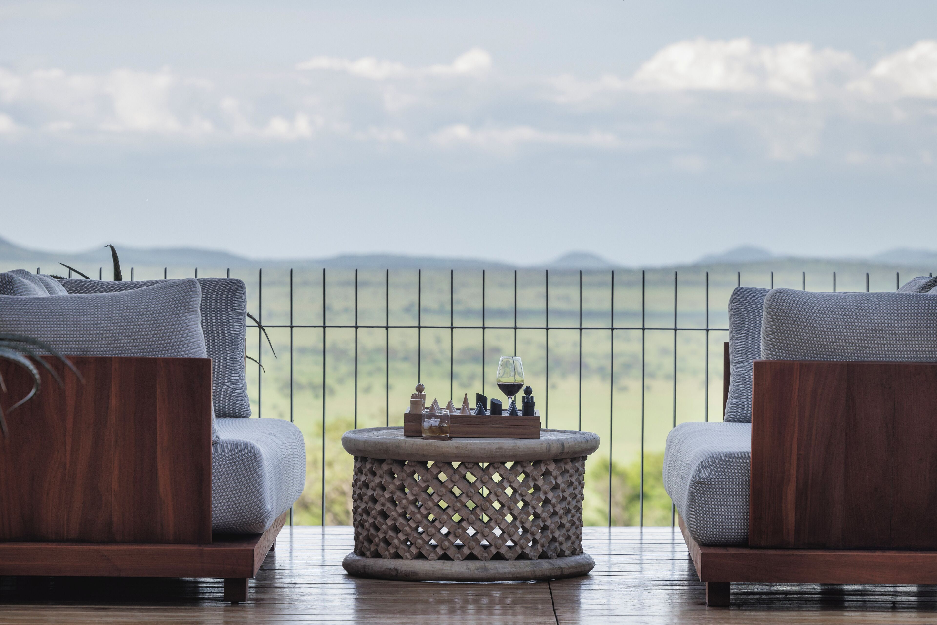 A balcony with two grey upholstered chairs and a round wooden table with a lattice design.