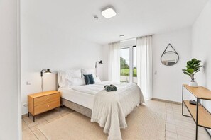 A bedroom with a bed, bedside table, lamp, mirror, and a potted plant. - The Serviced (Stuttgart)