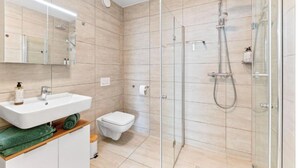 Un baño moderno con cabina de ducha de vidrio, un lavamanos blanco y un inodoro.