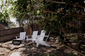 Relax in an outdoor space surrounded by trees, with three Adirondack chairs and a small table.