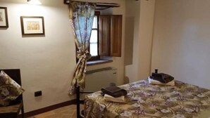 A bedroom with a bed, a chair, a window with curtains, and a small table with a book and a bottle. - MATRIMONIAL ROOM with private bathroom, (Radicondoli)